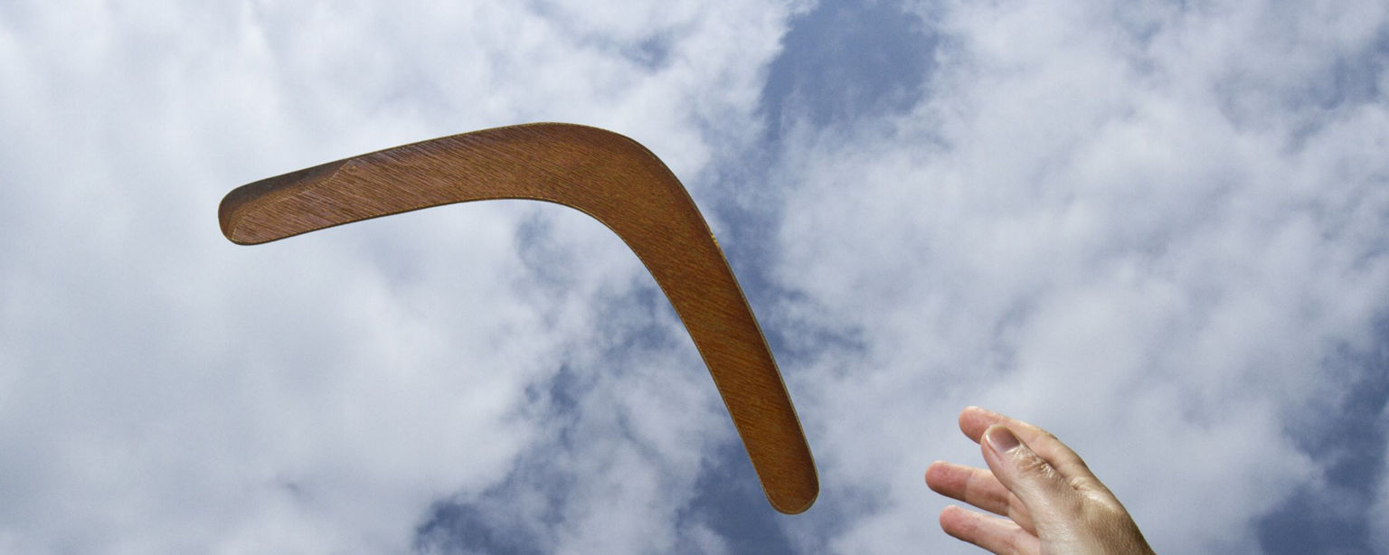 A boomerang flying against a blue sky, with a hand reaching up to catch it.